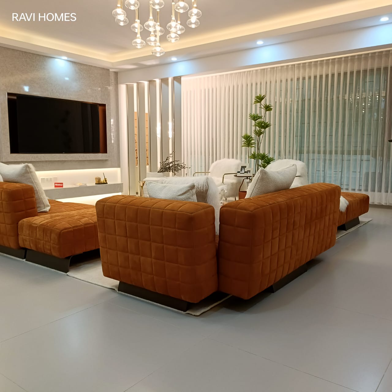 Royal Legend Residence luxury living room featuring orange upholstered sofas, modern chandelier, wall-mounted television, and floor-to-ceiling curtains.