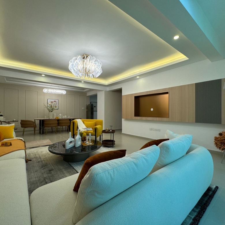 Royal Legend Residence spacious living room featuring cream sofas, yellow accent chair, black coffee table, decorative chandelier, and modern TV wall.