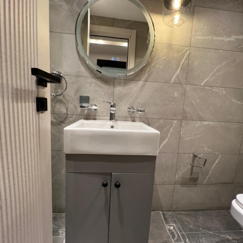 Symphony Residence bathroom vanity featuring a white ceramic washbasin, grey storage cabinet, round mirror and decorative pendant light.