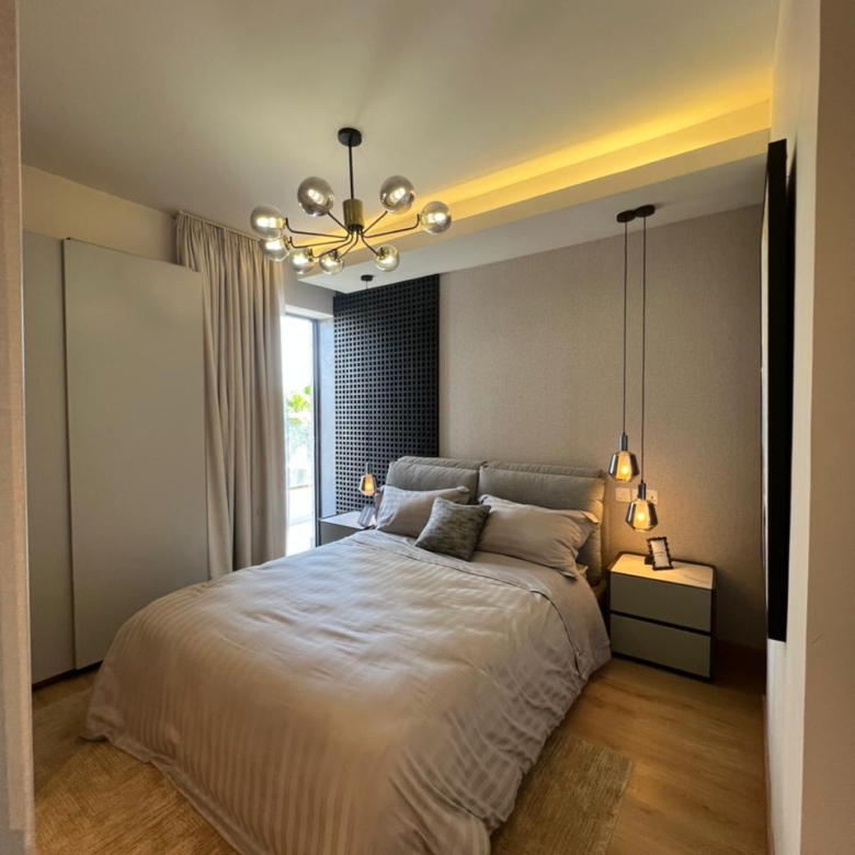 Symphony Residence modern bedroom featuring an upholstered double bed, decorative chandelier, bedside pendant lights, wardrobe and wooden flooring.