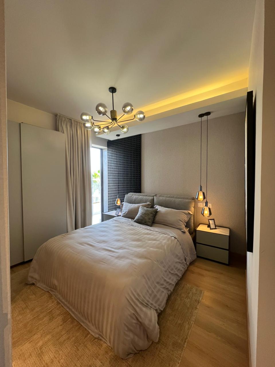 Symphony Residence modern bedroom featuring an upholstered double bed, decorative chandelier, bedside pendant lights, wardrobe and wooden flooring.