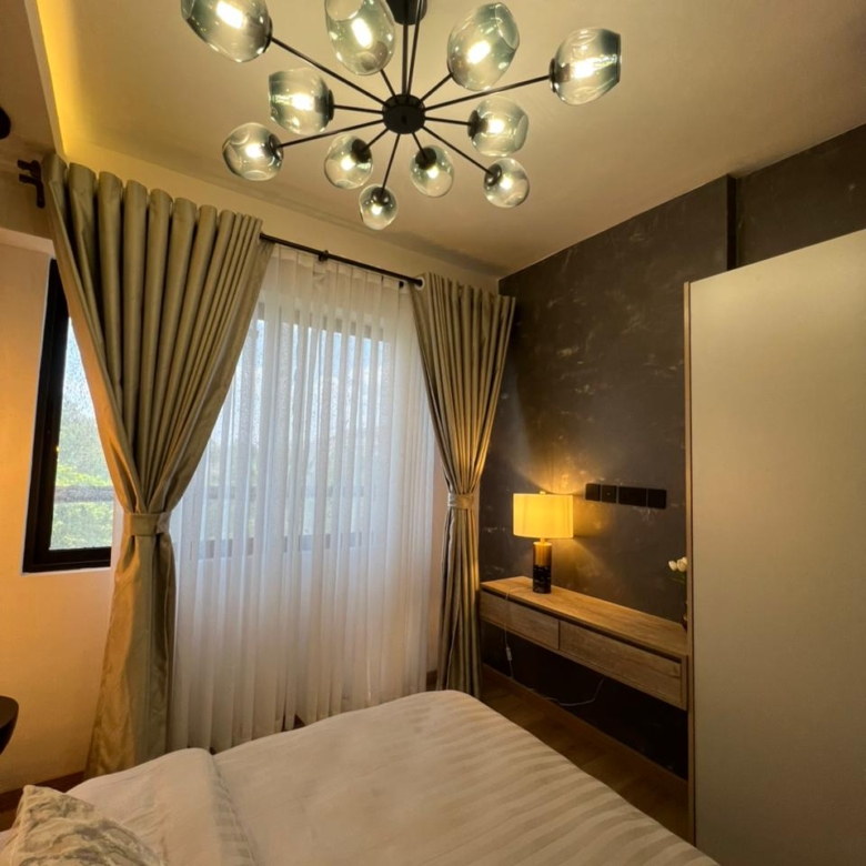 Symphony Residence bedroom interior featuring a modern glass chandelier, floor-length curtains, wooden dressing table, wardrobe and textured accent wall.