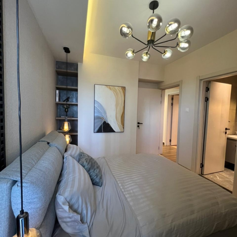 Symphony Residence bedroom featuring a large upholstered bed, pendant lighting, decorative ceiling chandelier, modern wall art and ensuite bathroom access.