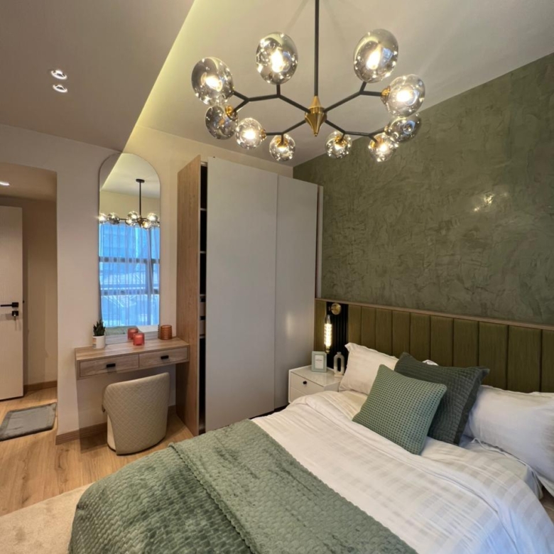 Symphony Residence bedroom featuring a green textured accent wall, upholstered bed, modern wardrobe, dressing table and decorative glass chandelier.