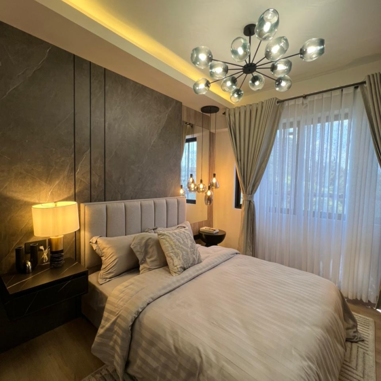 Symphony Residence modern bedroom with a grey upholstered headboard, marble-effect feature wall, glass chandelier, pendant lights and large window.