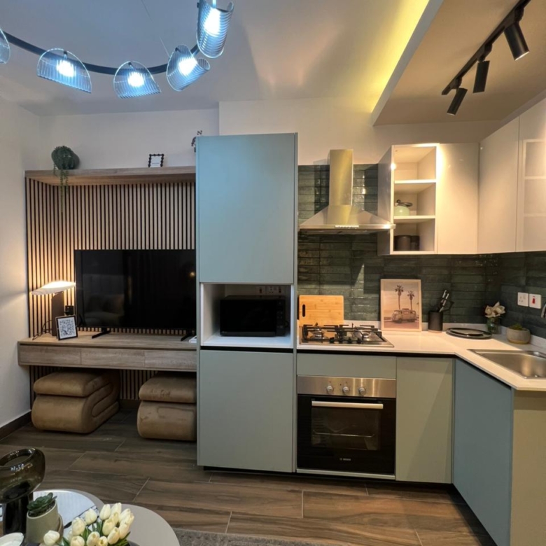 Symphony Residence modern open-plan kitchen featuring fitted cabinets, built-in oven, gas hob, extractor hood and an adjoining TV entertainment area.