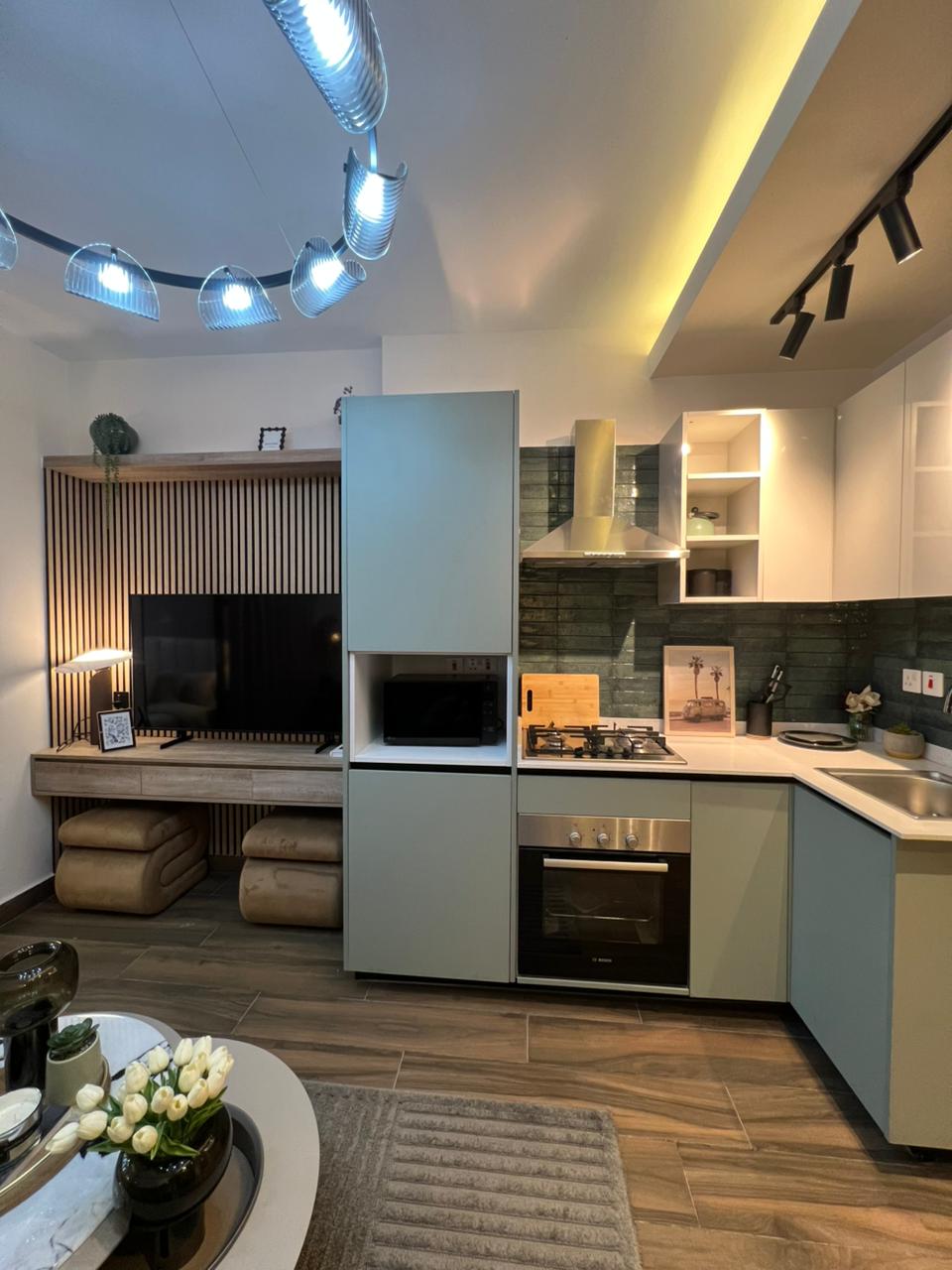 Symphony Residence modern open-plan kitchen featuring fitted cabinets, built-in oven, gas hob, extractor hood and an adjoining TV entertainment area.
