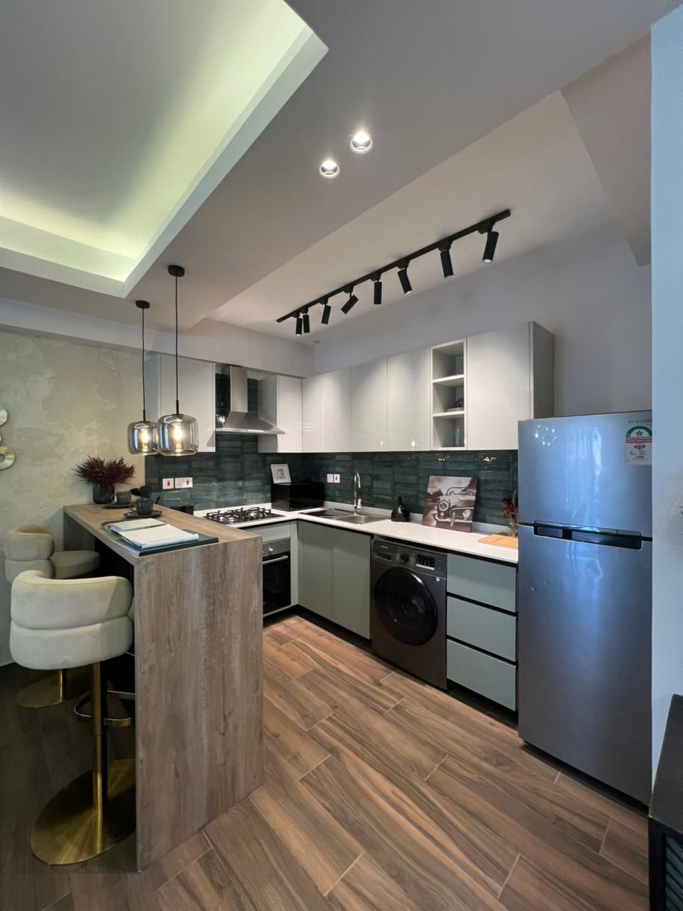 Symphony Residence fitted kitchen featuring a breakfast counter, modern cabinets, gas cooker, built-in oven, refrigerator and washing machine.