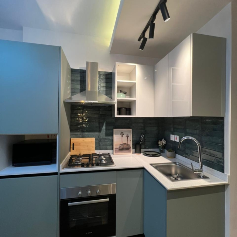 Symphony Residence kitchen featuring an L-shaped countertop, built-in oven, gas hob, stainless steel sink, extractor hood and fitted cabinets.