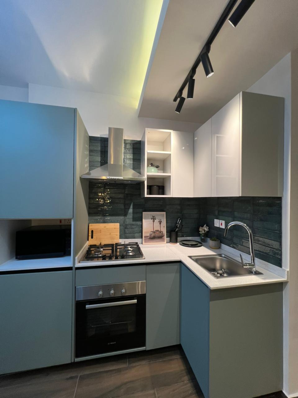 Symphony Residence kitchen featuring an L-shaped countertop, built-in oven, gas hob, stainless steel sink, extractor hood and fitted cabinets.