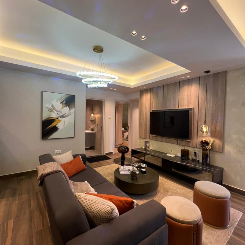 Symphony Residence modern living room featuring a grey sofa, mounted television, circular coffee table, decorative chandelier and wooden flooring.