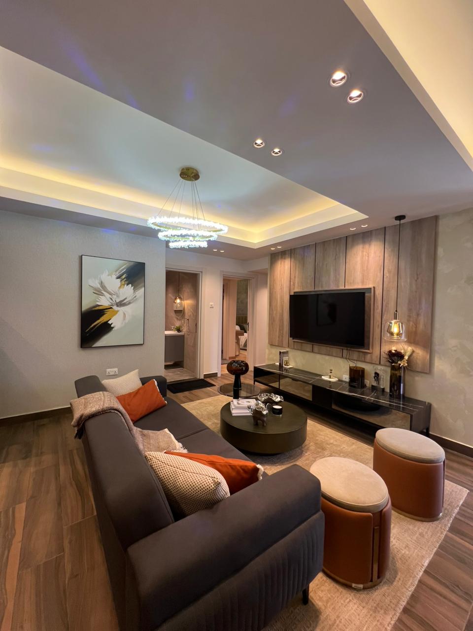 Symphony Residence modern living room featuring a grey sofa, mounted television, circular coffee table, decorative chandelier and wooden flooring.