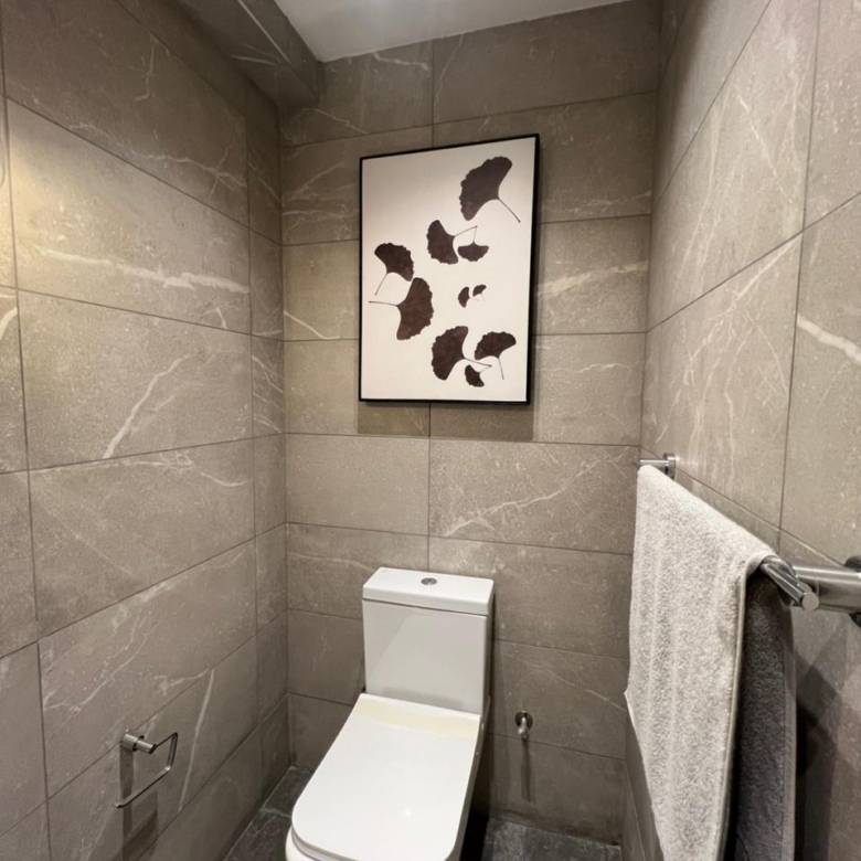 Symphony Residence modern toilet featuring grey marble-effect wall tiles, white ceramic WC, wall artwork and chrome towel rail.