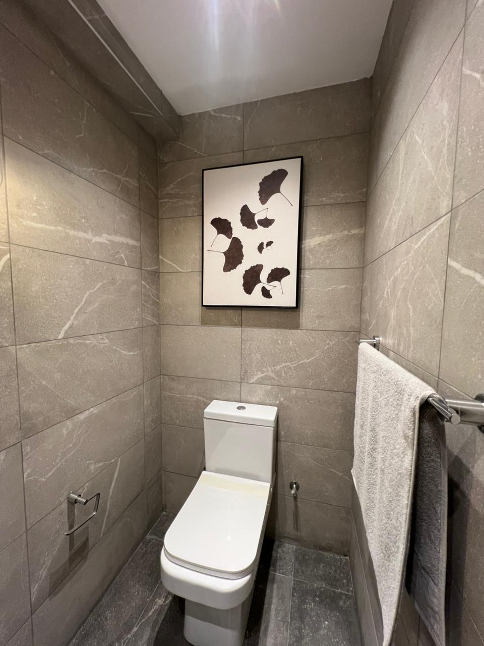 Symphony Residence modern toilet featuring grey marble-effect wall tiles, white ceramic WC, wall artwork and chrome towel rail.