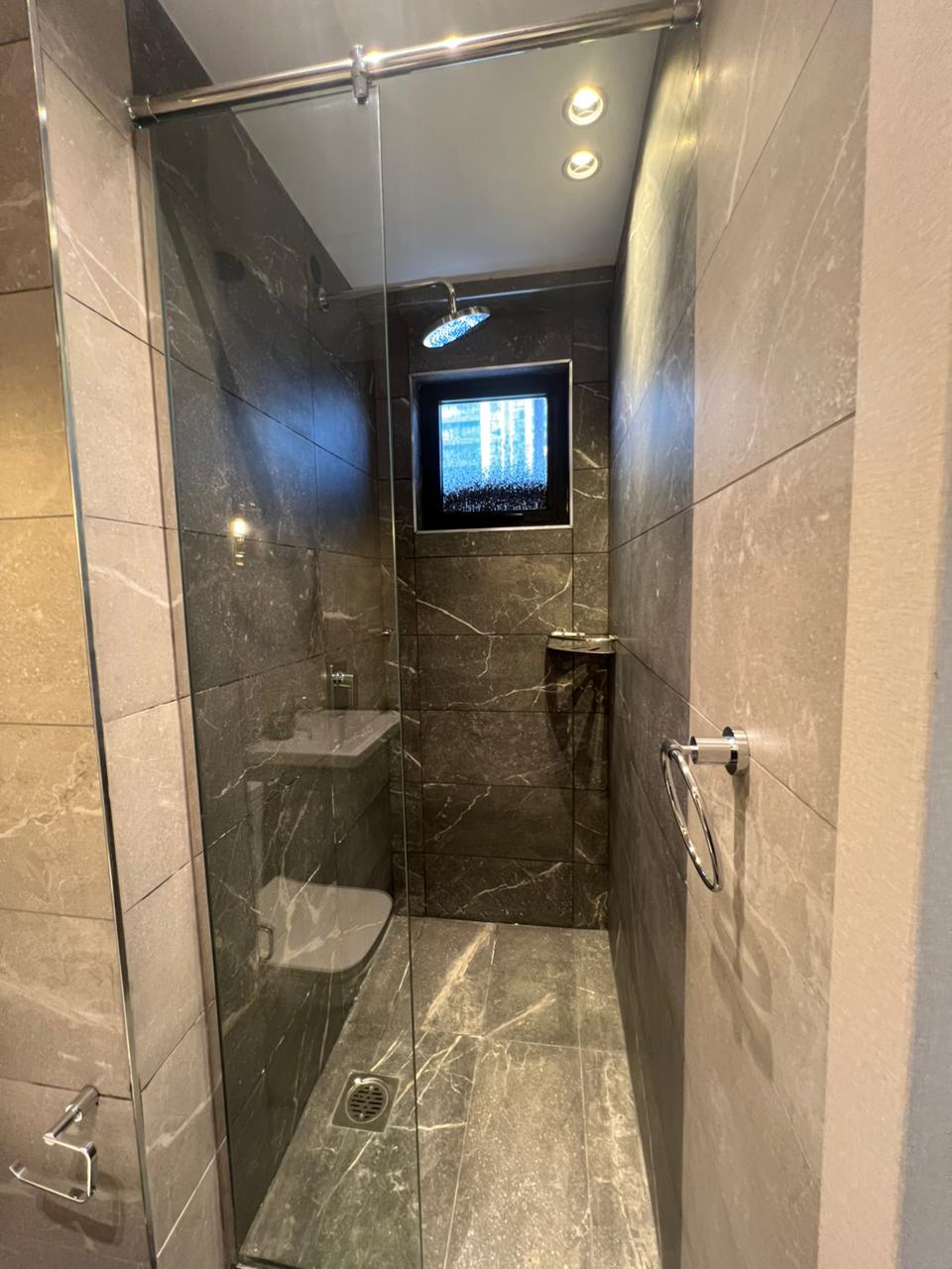 Symphony Residence modern shower enclosure featuring a glass partition, rainfall showerhead, dark marble-effect tiles and bathroom window.