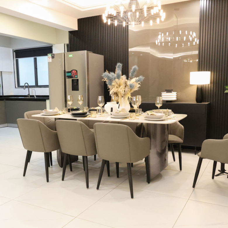 Modern dining area with a dining table, upholstered chairs, chandelier, and adjoining kitchen