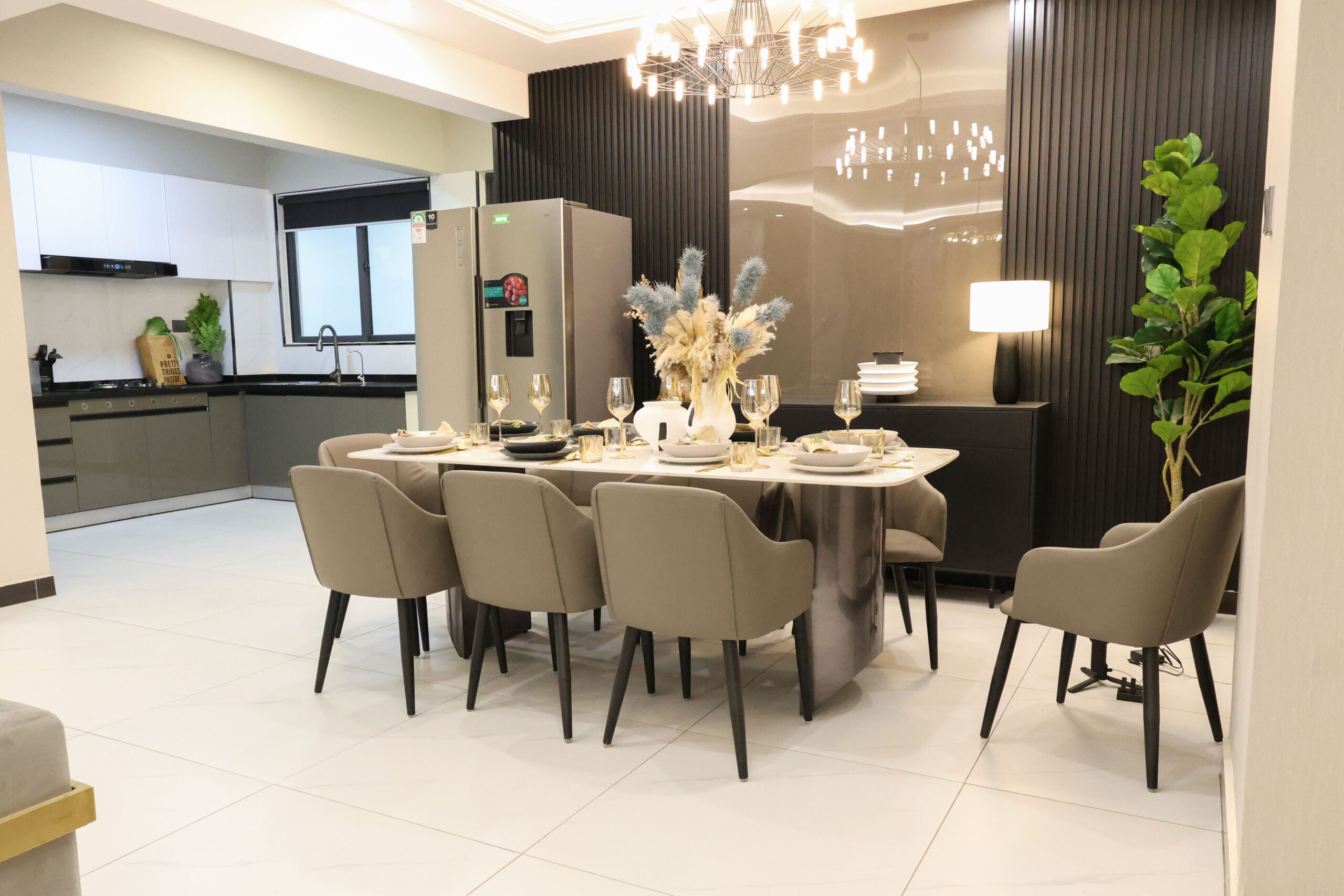 Modern dining area with a dining table, upholstered chairs, chandelier, and adjoining kitchen