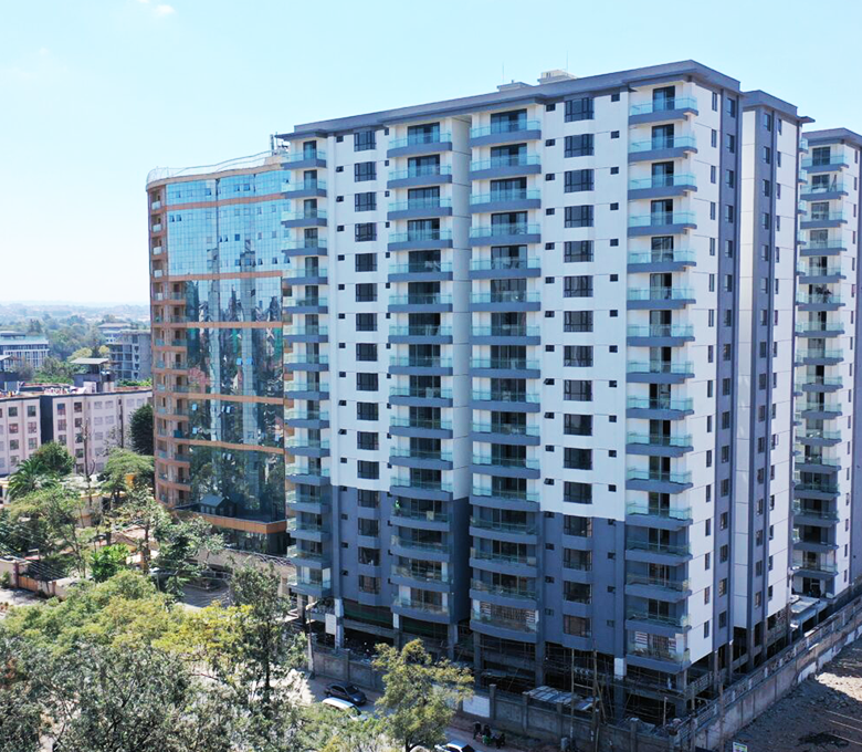 Exterior view of a modern multi-storey residential apartment building surrounded by trees and nearby buildings