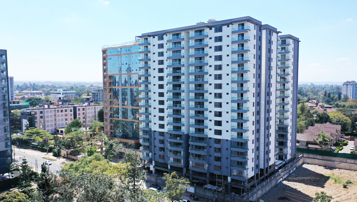 Exterior view of a modern multi-storey residential apartment building surrounded by trees and nearby buildings