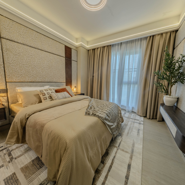 Montbleu apartments modern 1-bedroom interior featuring a double bed, decorative padded headboard wall, bedside lighting, full-length curtains, and contemporary bedroom furniture.