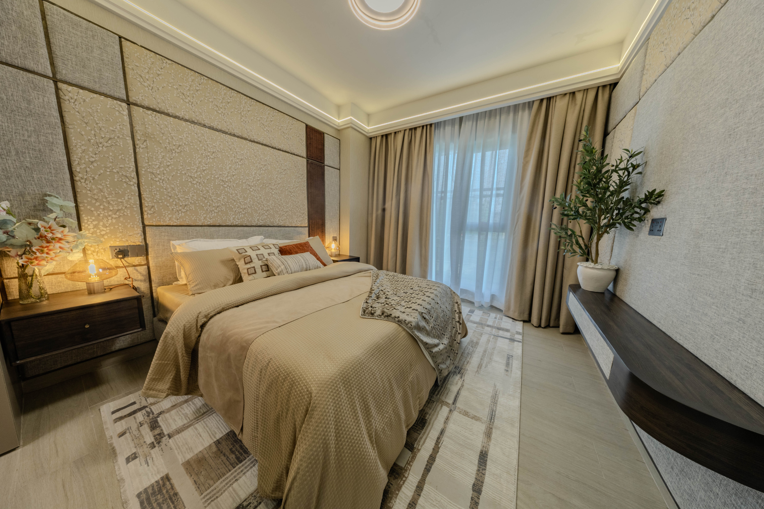 Montbleu apartments modern 1-bedroom interior featuring a double bed, decorative padded headboard wall, bedside lighting, full-length curtains, and contemporary bedroom furniture.