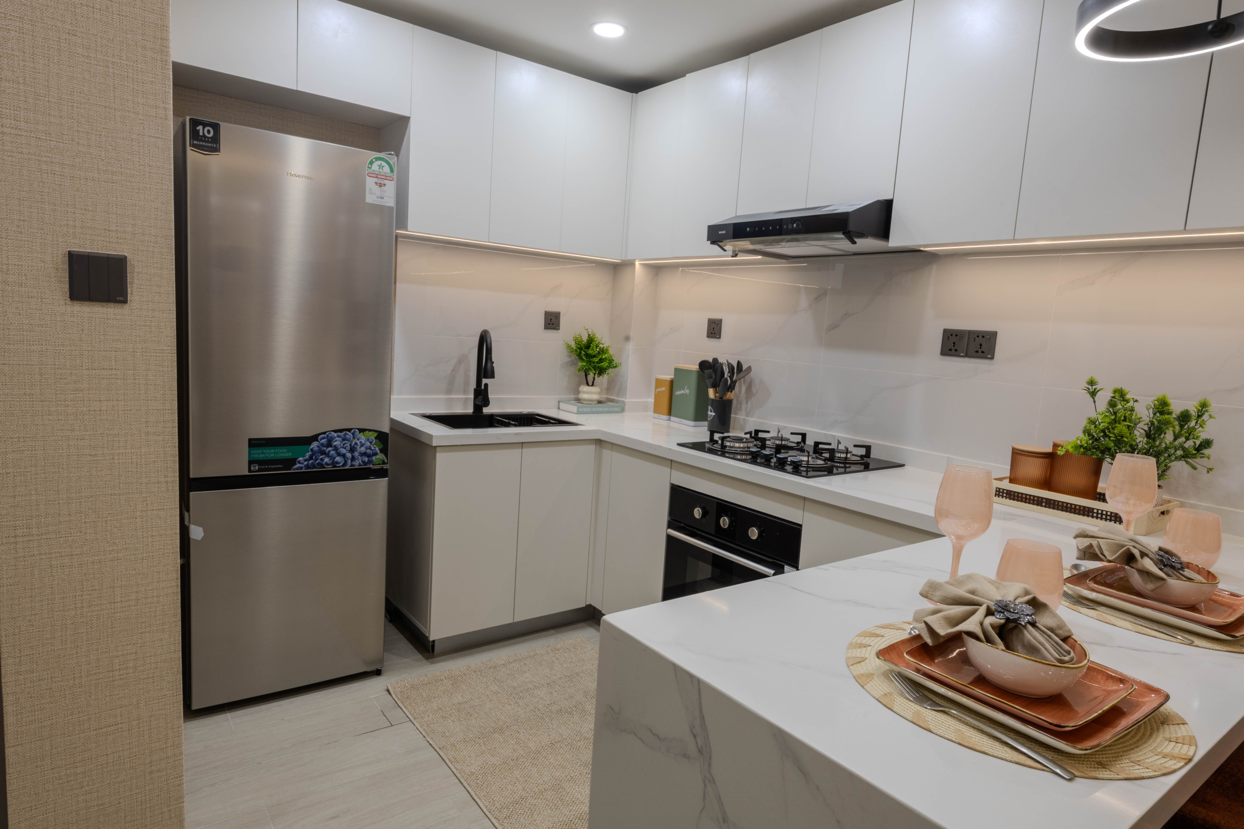 Montbleu apartments 1-bedroom modern kitchen featuring white fitted cabinets, stainless steel refrigerator, black sink, gas hob, extractor hood, and stylish breakfast counter.