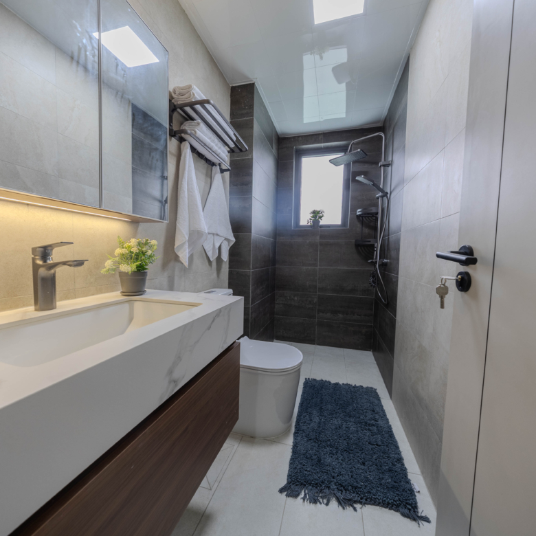 Montbleu apartments modern bathroom featuring a marble-effect vanity sink, illuminated mirror cabinet, rainfall shower, handheld shower, contemporary toilet, and grey tiled walls.