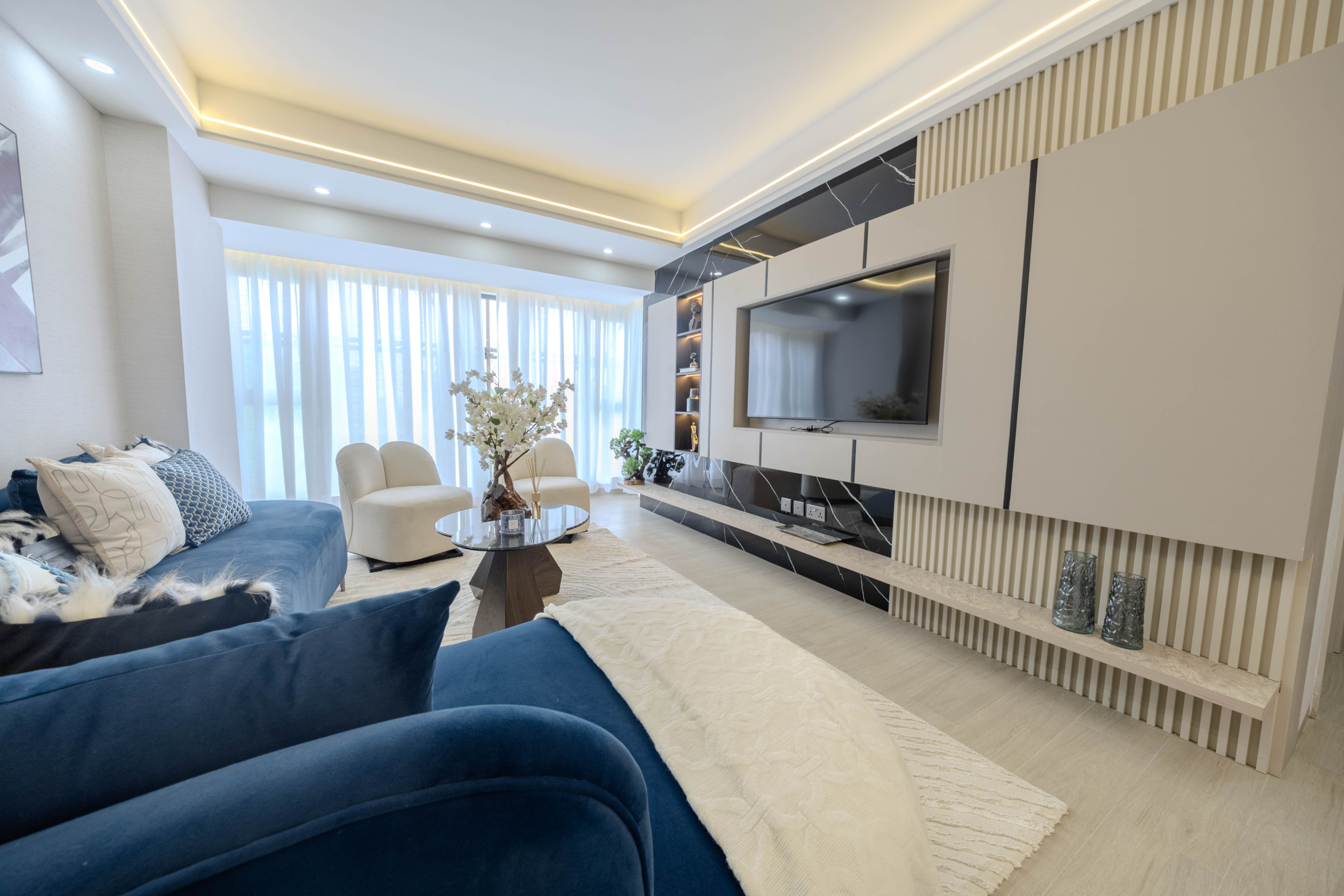 Montbleu apartments 2-bedroom open-plan living and dining area featuring a blue upholstered sofa, glass dining table, modern pendant lights, entertainment wall, and large windows.