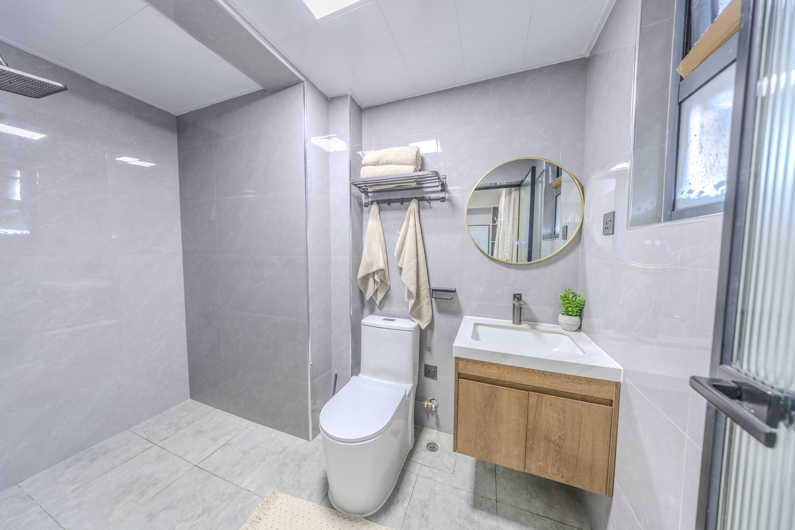 Marina Bay Phase III bathroom interior with rainfall shower, modern toilet, floating wooden vanity, and circular mirror.