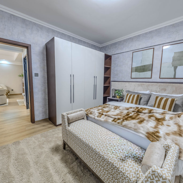 Marina Bay Phase III bedroom featuring a double bed, built-in white wardrobe, upholstered bench, and wooden flooring.