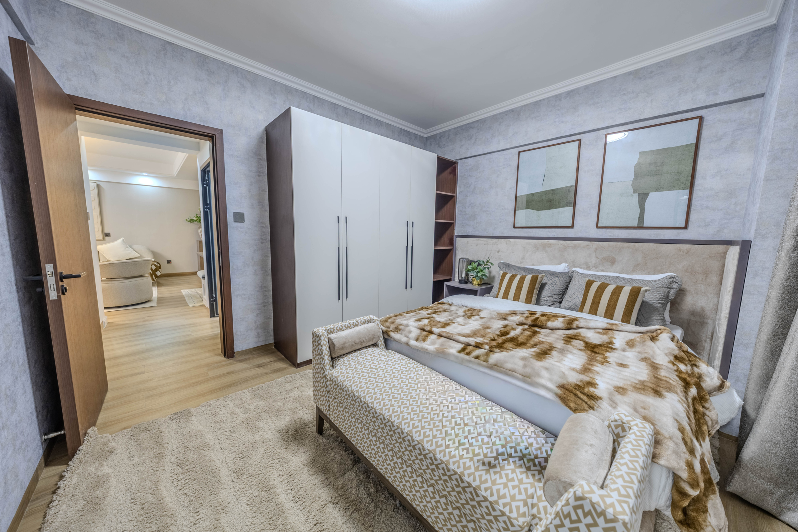 Marina Bay Phase III bedroom featuring a double bed, built-in white wardrobe, upholstered bench, and wooden flooring.