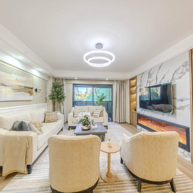 Marina Bay Phase III elegant living room featuring cream sofas, marble-look TV wall, electric fireplace, wooden display shelves, and balcony doors.