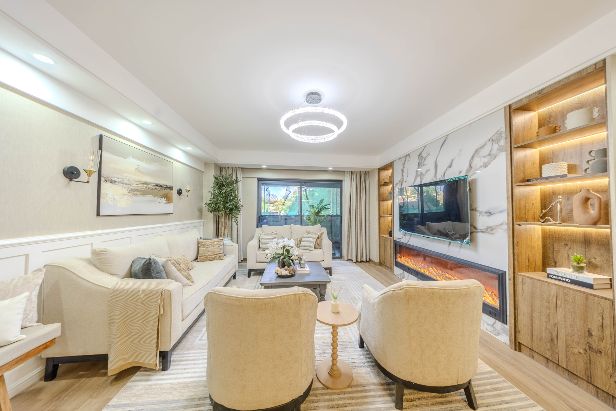 Marina Bay Phase III elegant living room featuring cream sofas, marble-look TV wall, electric fireplace, wooden display shelves, and balcony doors.