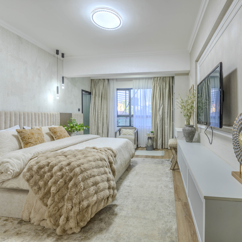Marina Bay Phase III spacious bedroom with upholstered bed, wall-mounted television, decorative lighting, and large window.