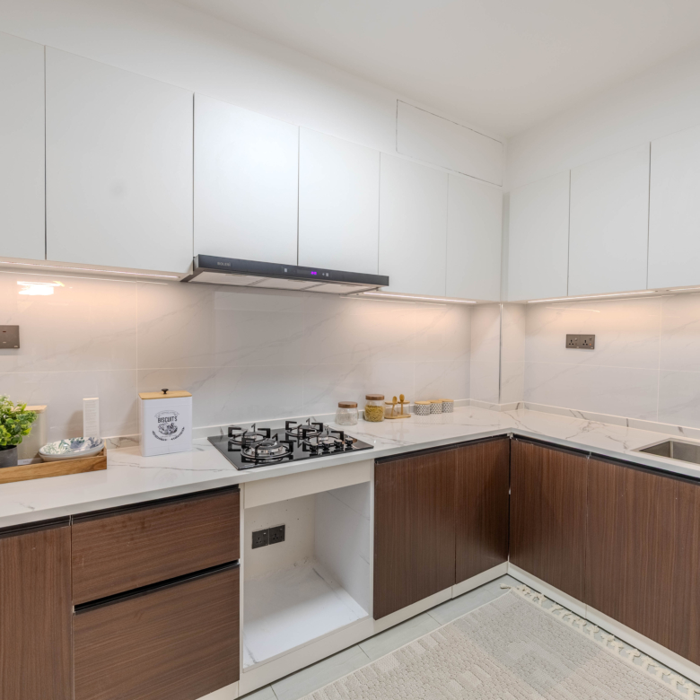 Marina Bay Phase III L-shaped kitchen featuring white cabinets, wooden lower cupboards, gas hob, stainless steel sink, and marble-look surfaces.