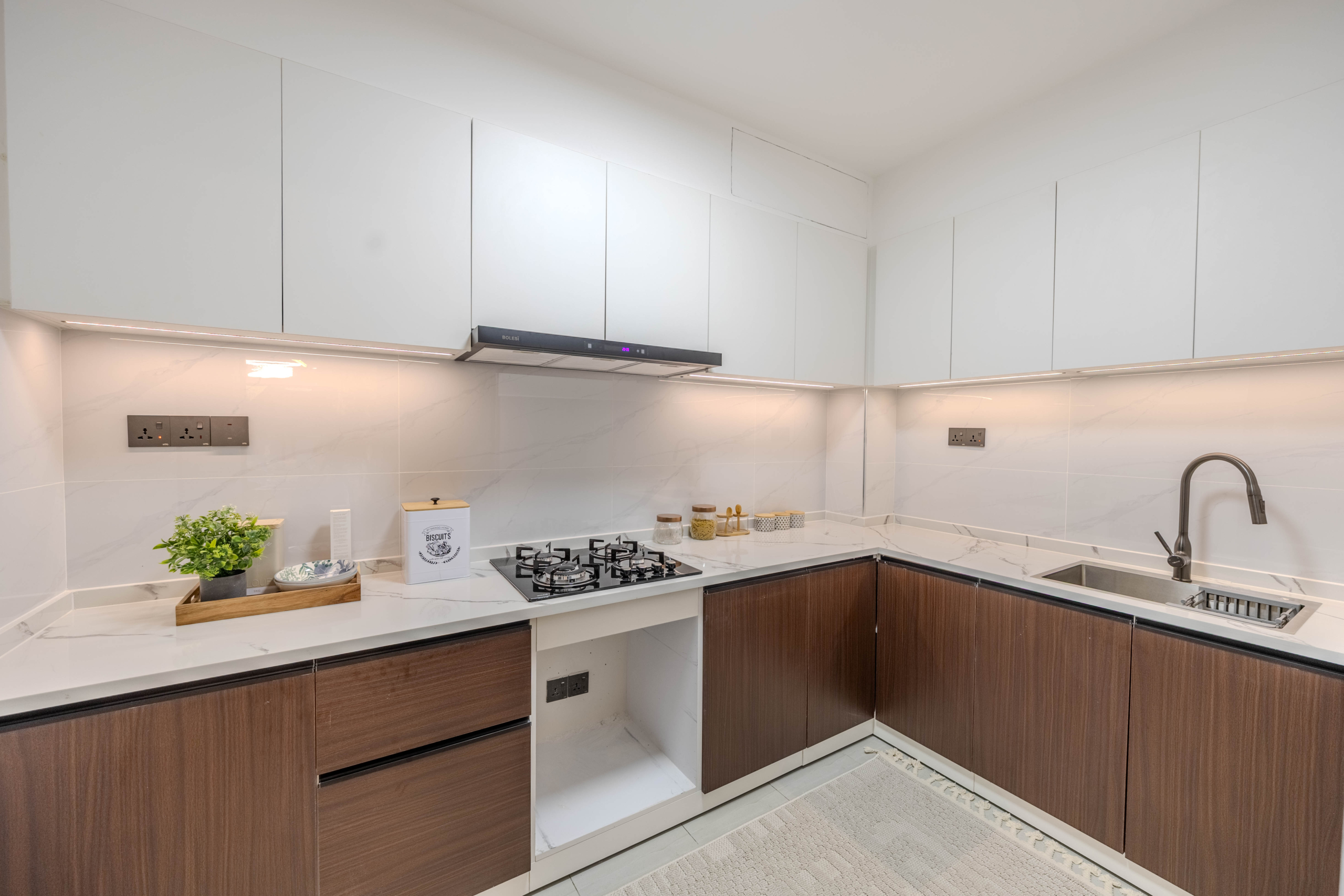 Marina Bay Phase III L-shaped kitchen featuring white cabinets, wooden lower cupboards, gas hob, stainless steel sink, and marble-look surfaces.