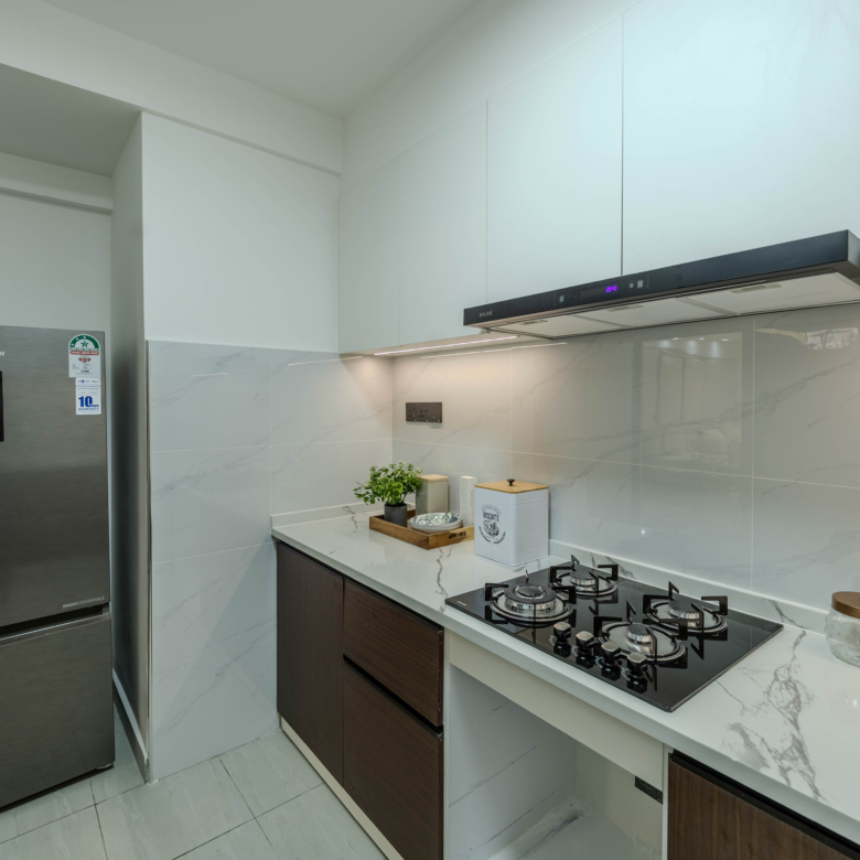 Marina Bay Phase III modern kitchen with gas hob, extractor hood, refrigerator, wooden cabinets, and marble-look countertops.