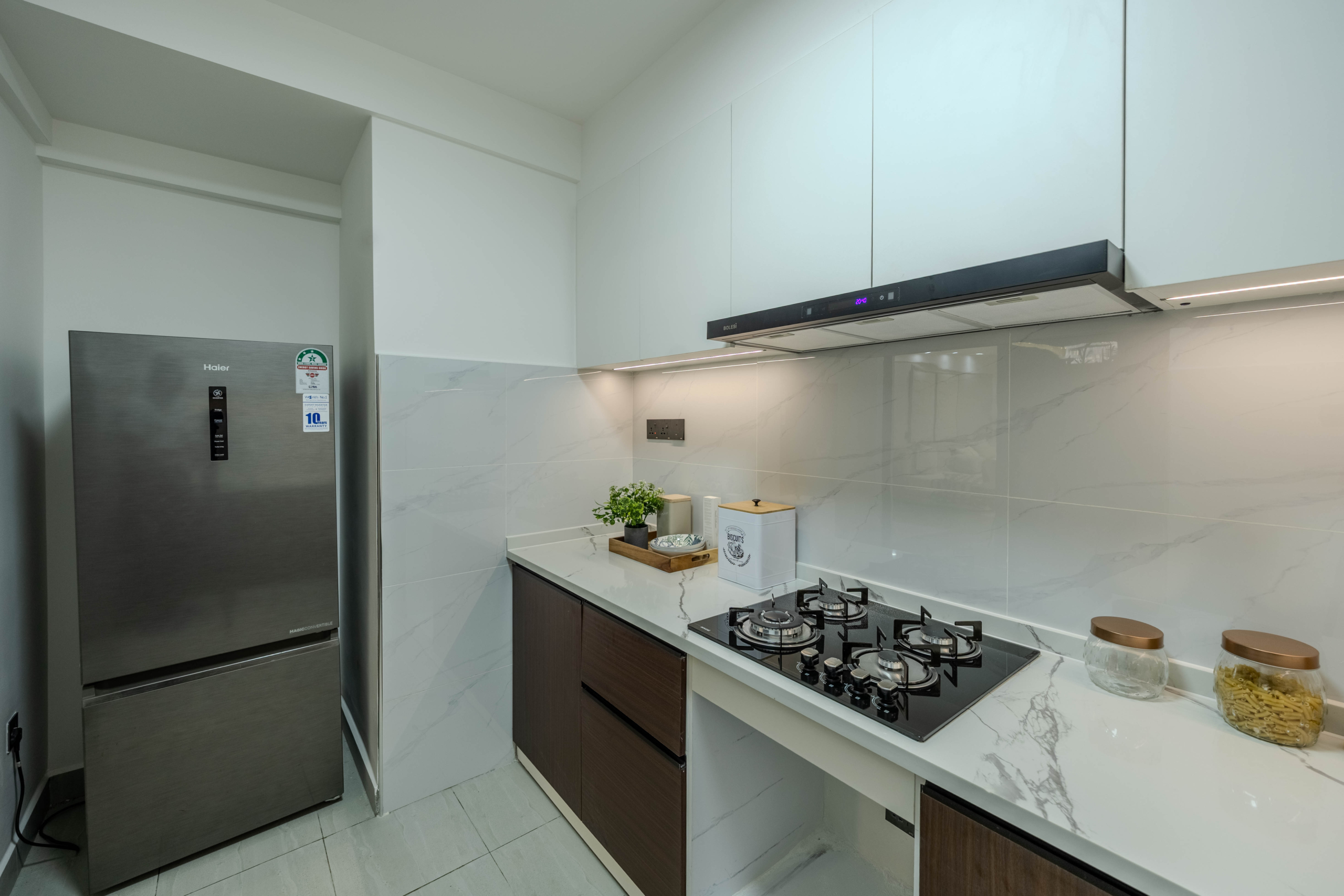 Marina Bay Phase III modern kitchen with gas hob, extractor hood, refrigerator, wooden cabinets, and marble-look countertops.