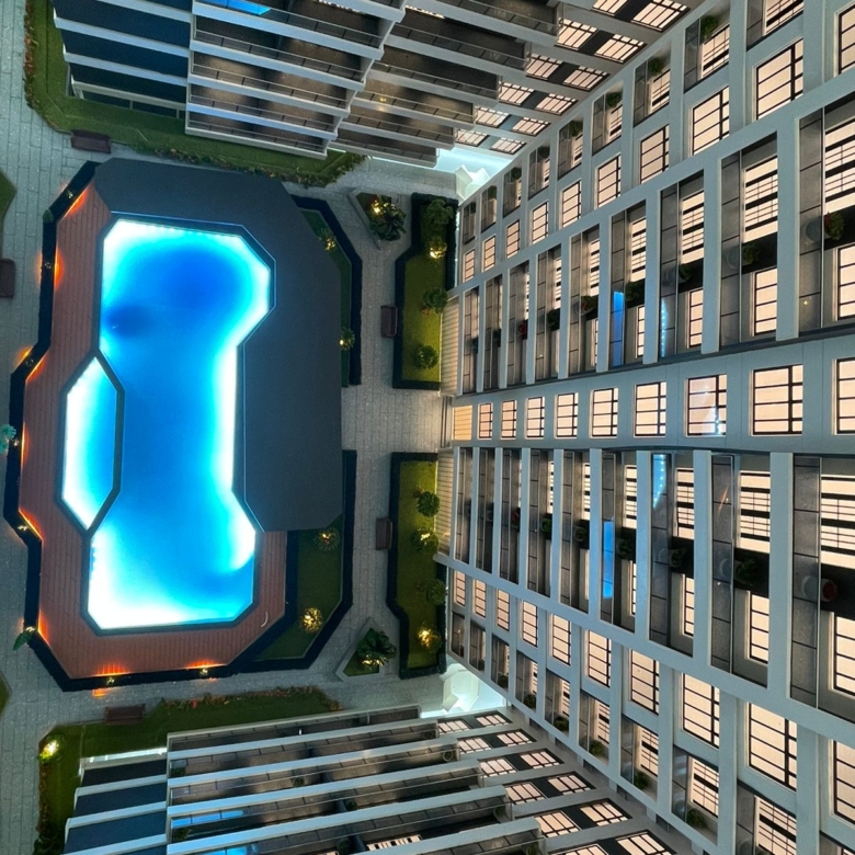 Metricon Oasis aerial view showing an illuminated swimming pool, landscaped courtyard and modern residential apartment buildings.