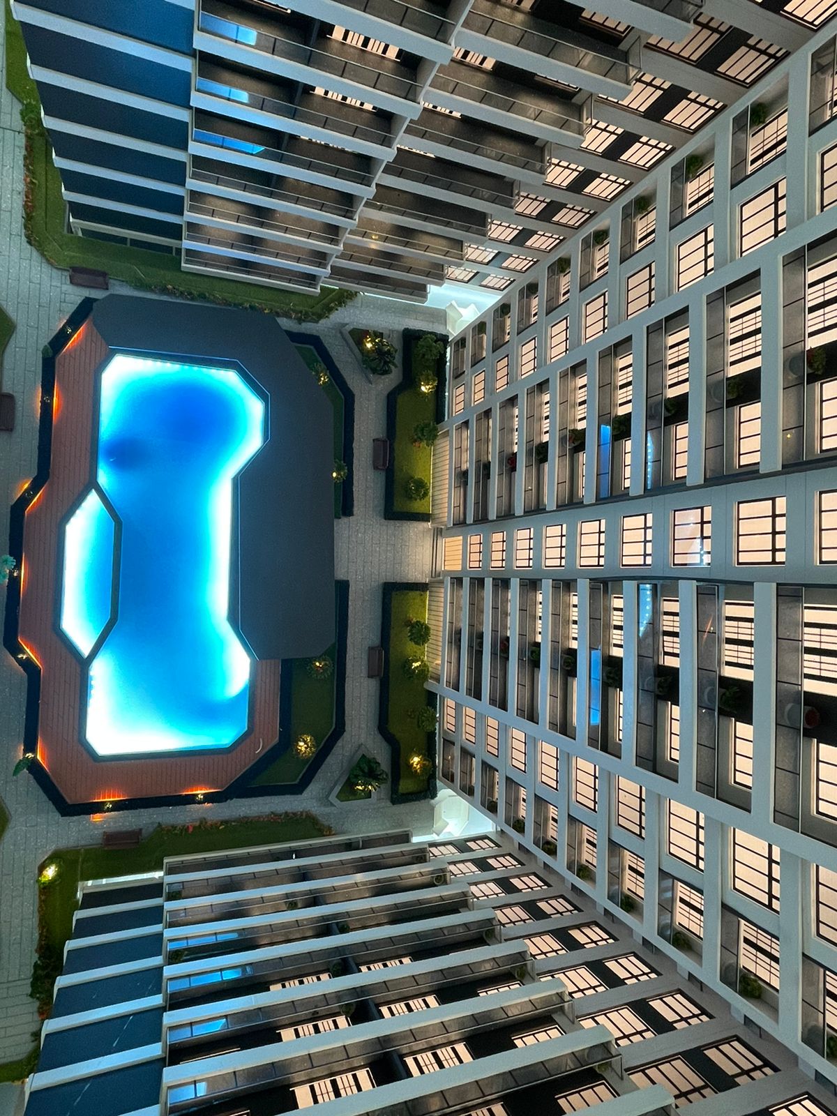 Metricon Oasis aerial view showing an illuminated swimming pool, landscaped courtyard and modern residential apartment buildings.