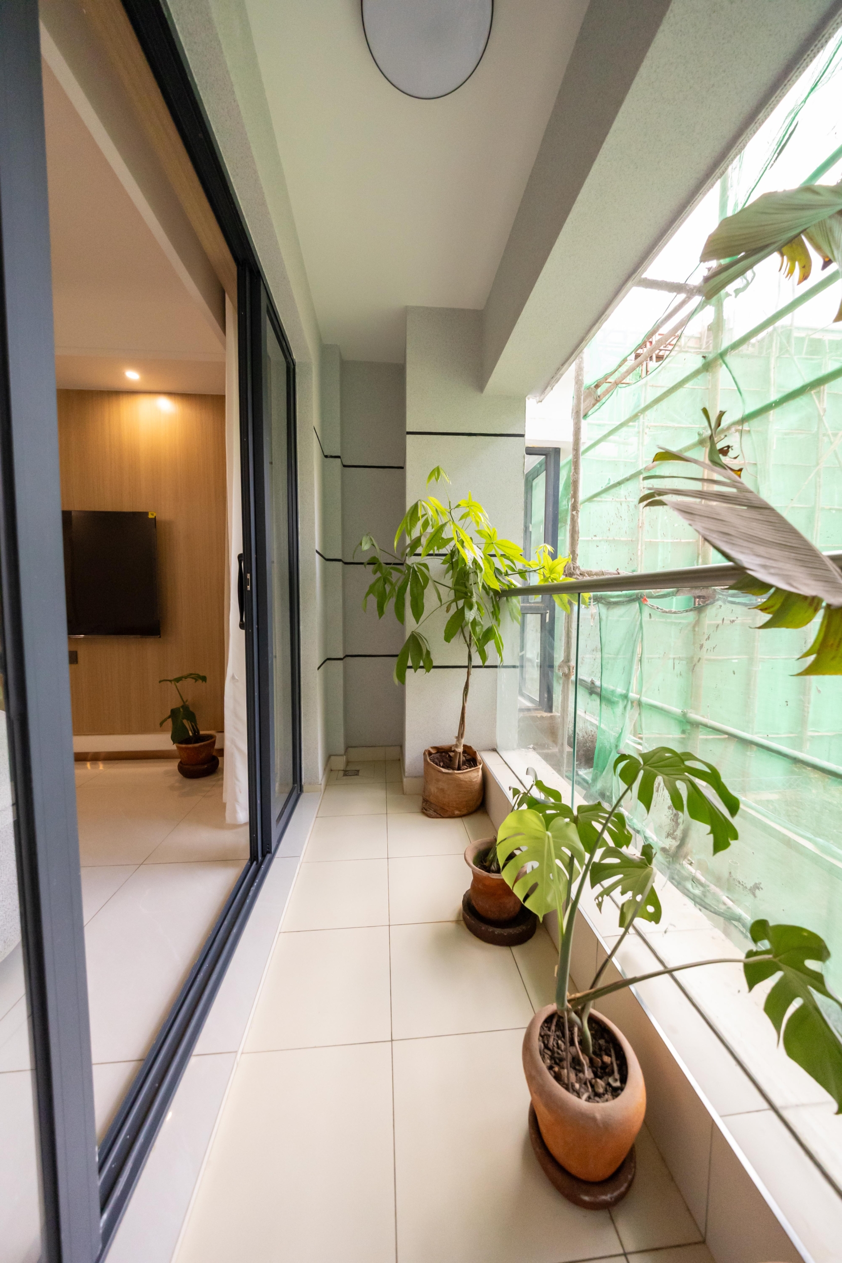 Rhapta One Residency private apartment balcony with tiled flooring, glass railings, potted plants, and sliding glass doors.