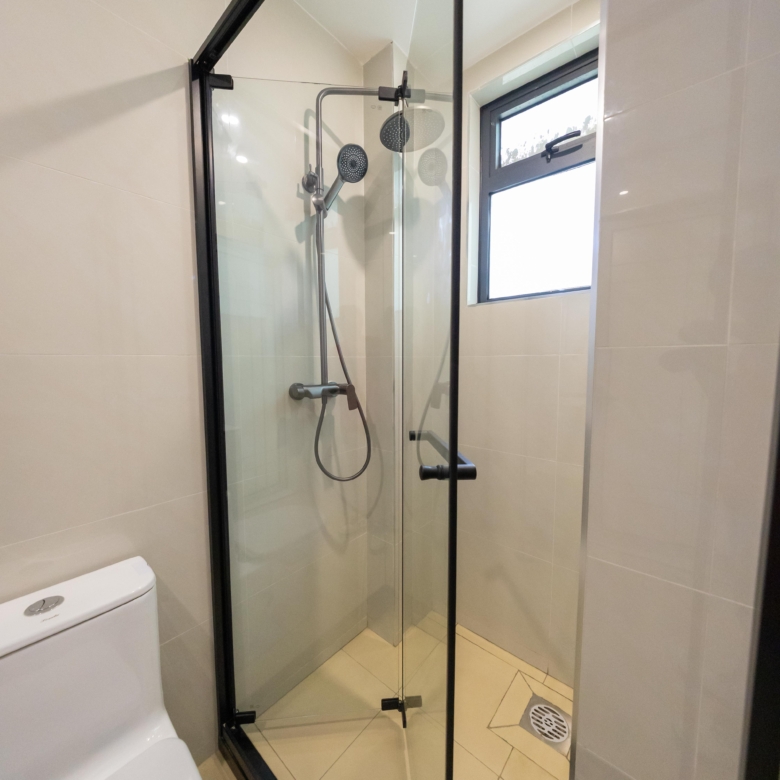Rhapta One Residency bathroom featuring a black-framed glass shower cubicle, rainfall showerhead, handheld shower, and ventilation window.