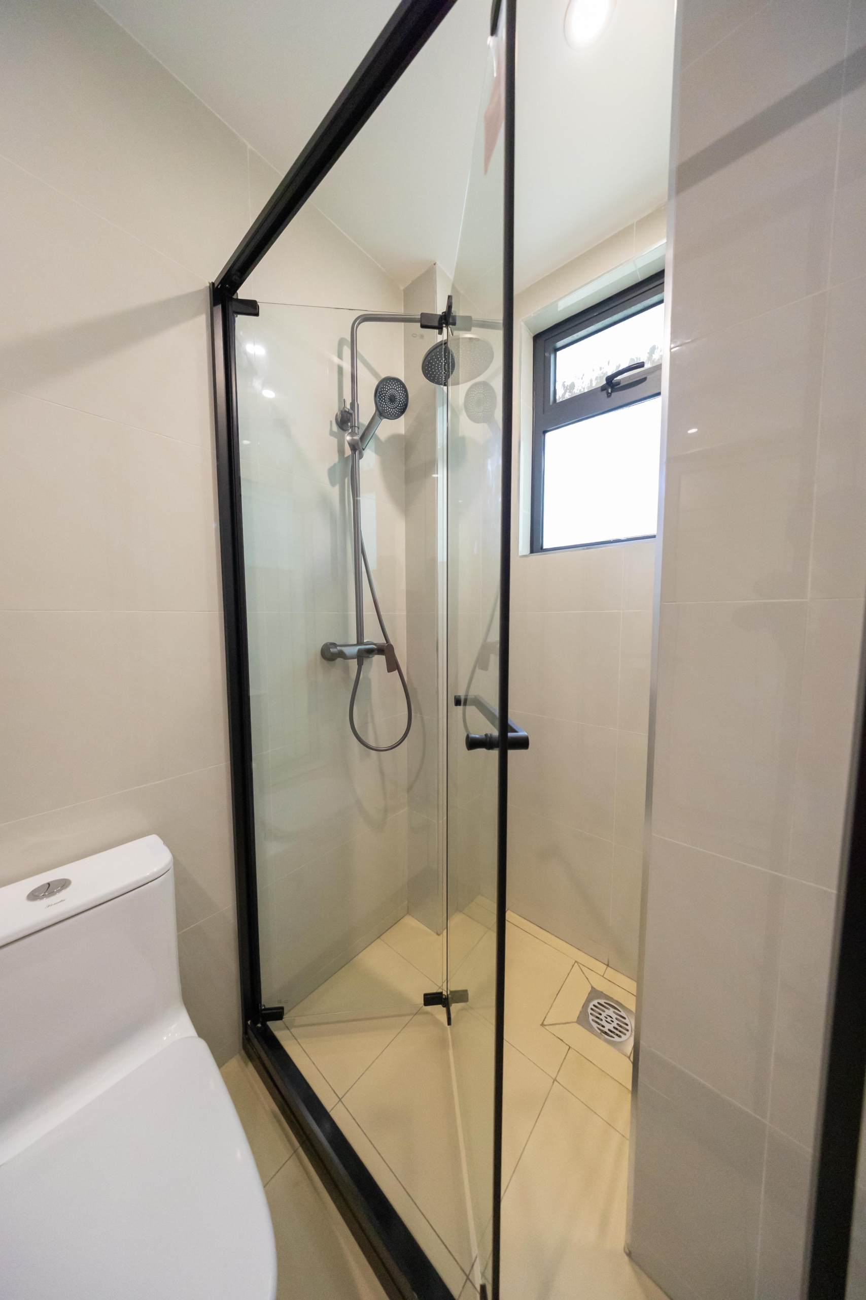 Rhapta One Residency bathroom featuring a black-framed glass shower cubicle, rainfall showerhead, handheld shower, and ventilation window.