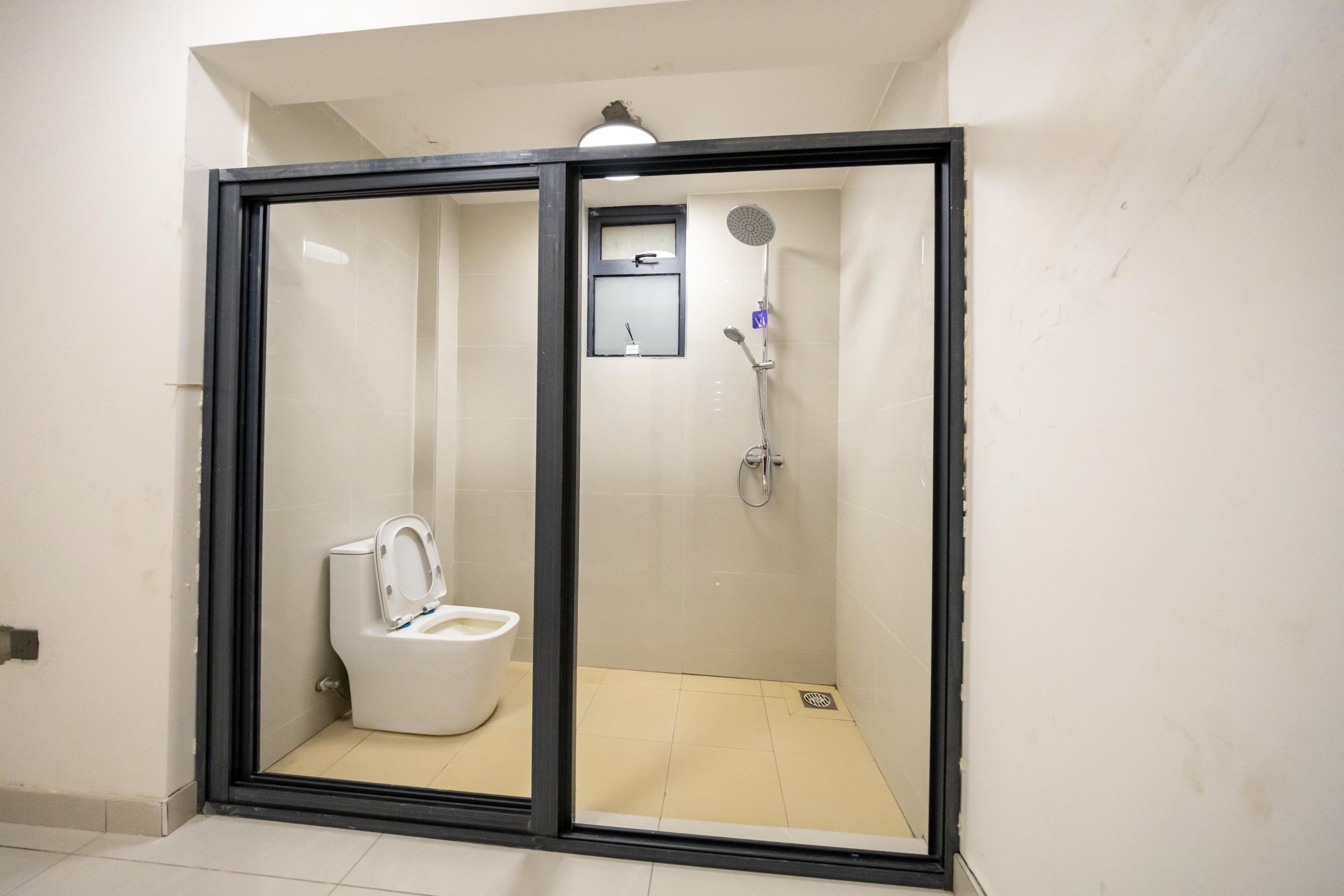 Rhapta One Residency modern bathroom with black-framed glass shower enclosure, white toilet, rainfall shower, and tiled walls.