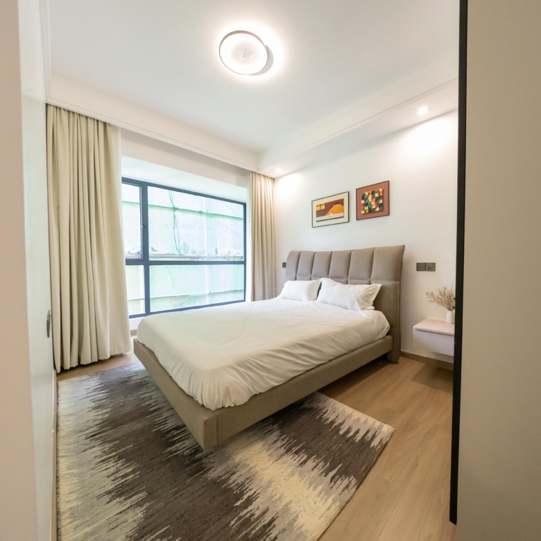 Rhapta One Residency stylish bedroom with upholstered bed, white bedding, large window, floating bedside table, and wooden flooring.