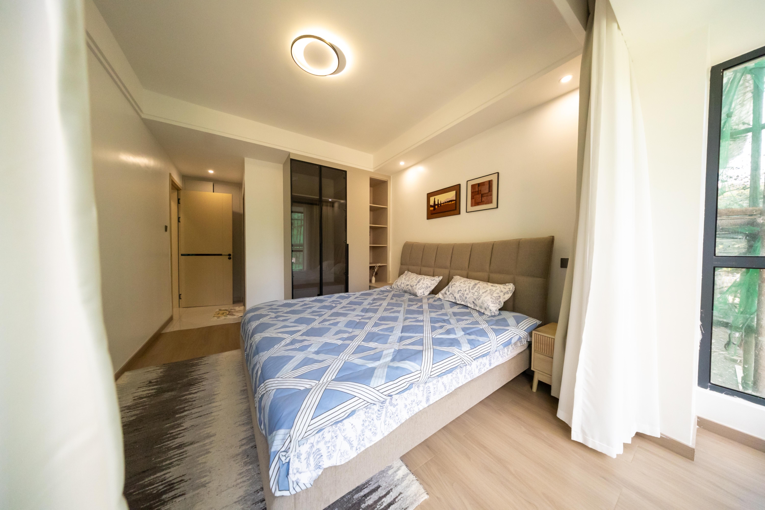 Rhapta One Residency spacious bedroom with double bed, blue patterned bedding, fitted wardrobes, bedside cabinet, and wooden flooring.