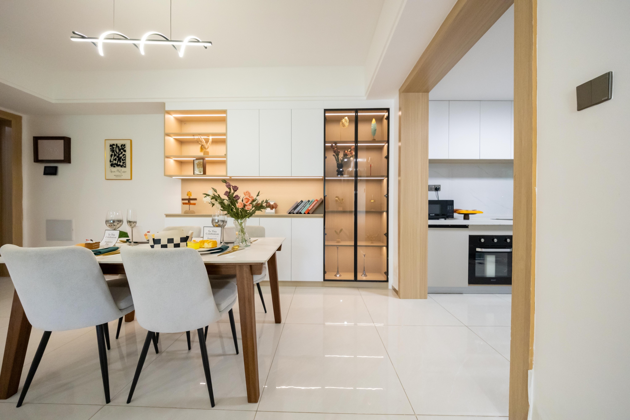 Rhapta One Residency elegant dining room with four-seater table, illuminated shelving, glass-fronted display cabinet, and kitchen access.