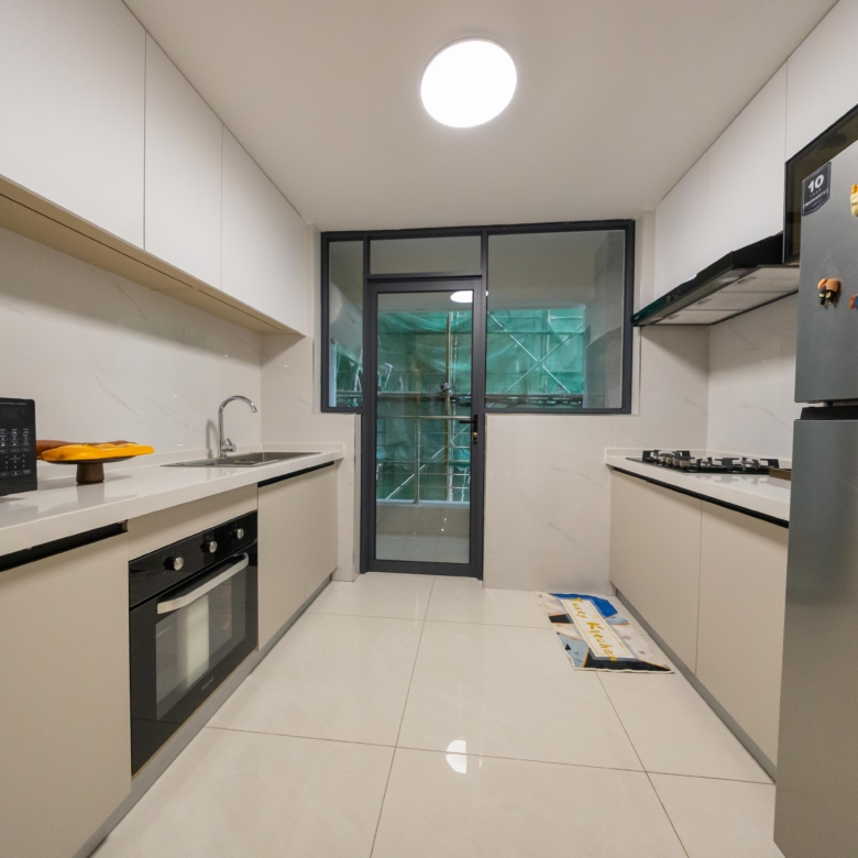Rhapta One Residency modern fitted kitchen with white cabinets, built-in oven, microwave, gas hob, refrigerator, and utility door.