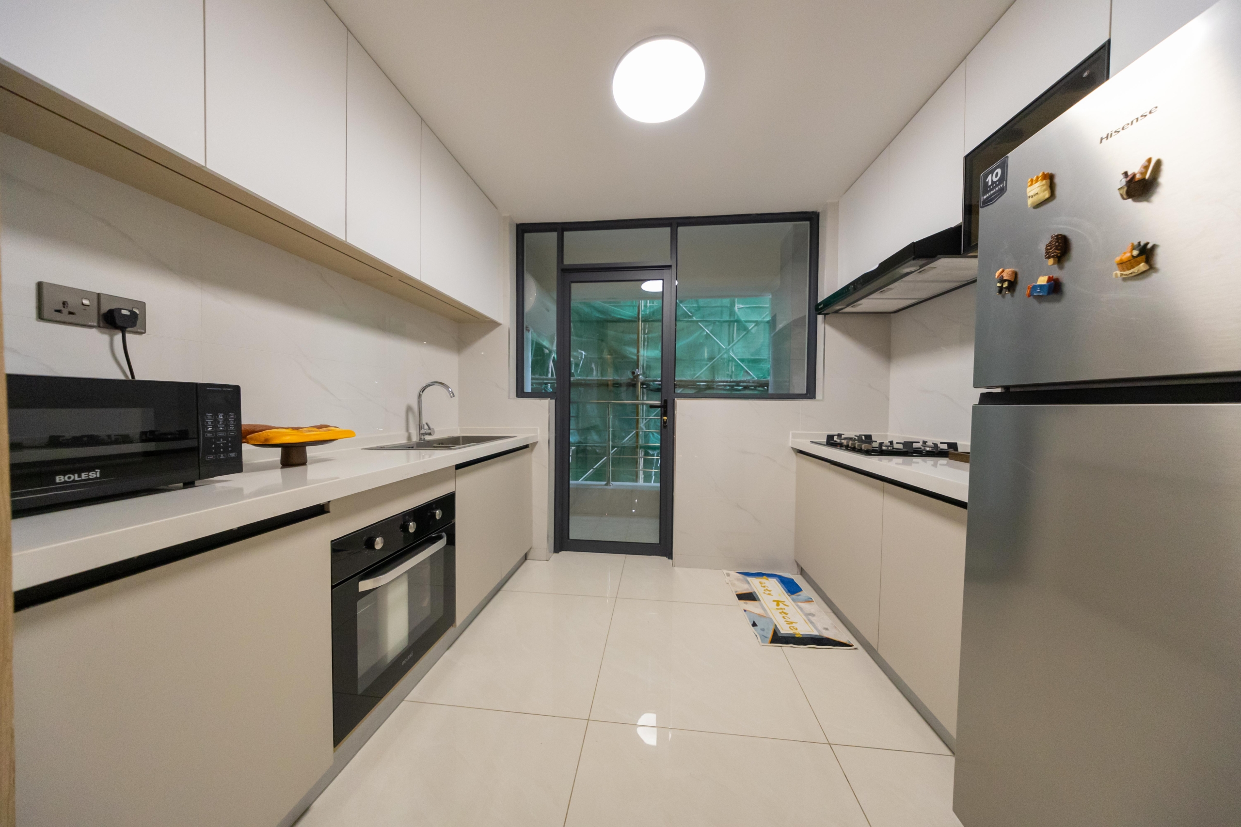 Rhapta One Residency modern fitted kitchen with white cabinets, built-in oven, microwave, gas hob, refrigerator, and utility door.