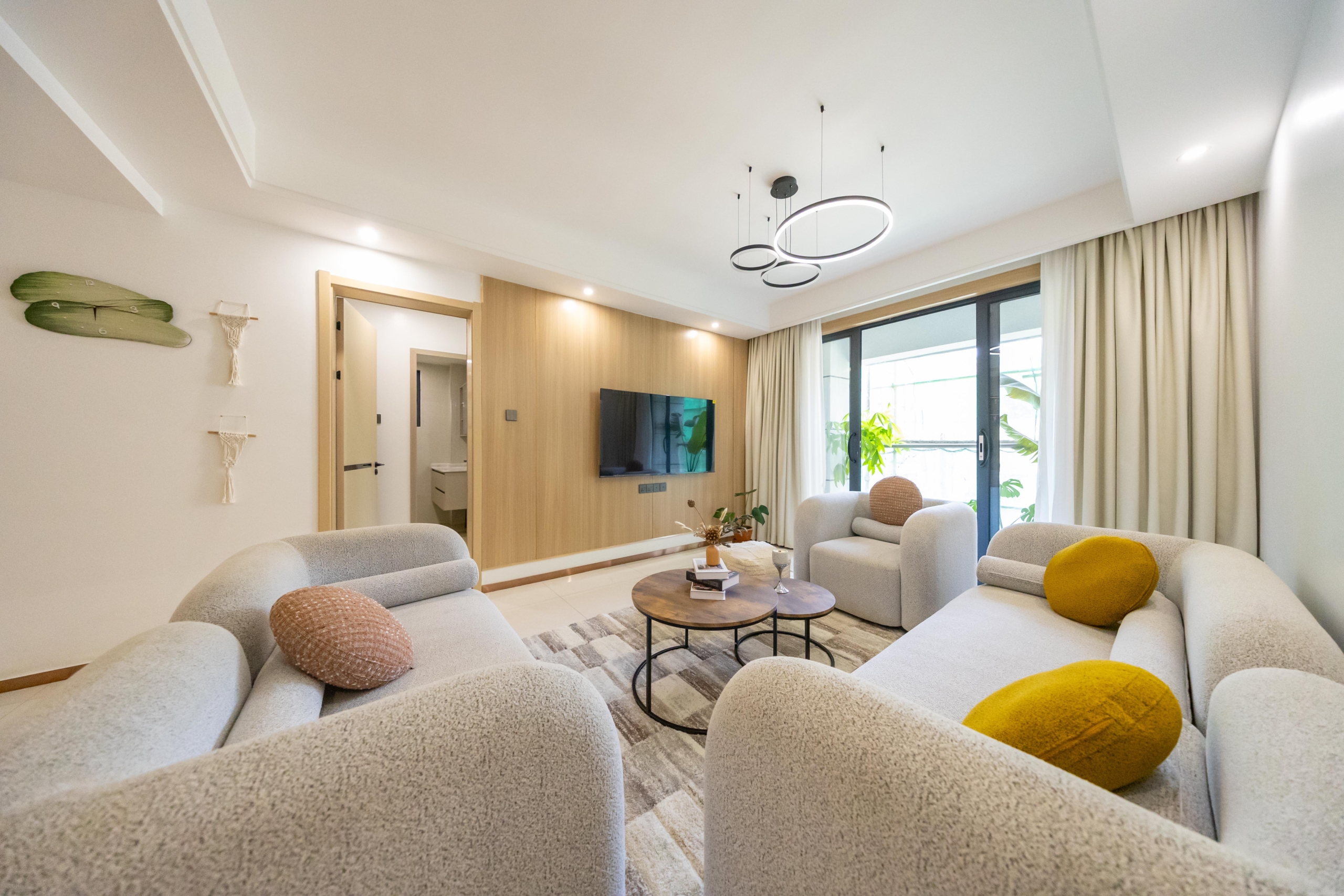 Rhapta One Residency modern living room with cream sofas, wooden TV feature wall, circular coffee tables, and sliding balcony doors.